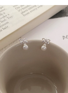 Detail of silver bow earrings with round white pearls on a ceramic cup rim