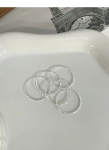 Detail of thin S925 silver rings with sparkling textures on a white ceramic tray