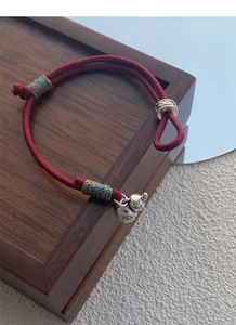 Close-up of S999 silver gourd pendant on a red braided rope bracelet over a wooden box