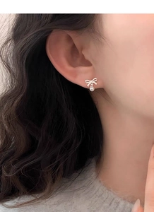 Close-up of a silver bow earring with a round white pearl on a female model's ear