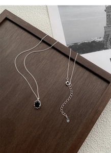 Detailed close-up of 925 silver necklace with black oval zircon pendant on wood