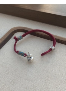 Detailed view of red braided bracelet with silver double gourds and fortune beads