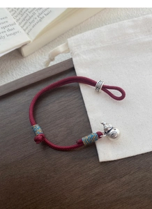 Close-up of red braided rope bracelet with silver gourd pendant and engraved Fu character