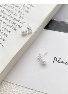 Detailed view of silver bow-shaped stud earrings with glossy white pearls on a magazine