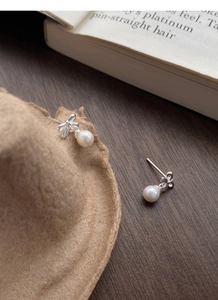 Detail of S925 sterling silver bow earrings with round white pearls on a textured background