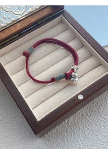 Macro shot of S999 silver gourd charm on red woven bracelet in a wooden gift box