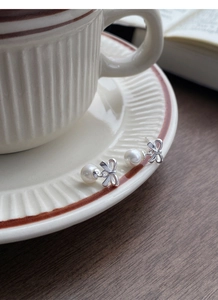 Macro shot of silver bow pearl earrings resting on a cream ceramic coffee saucer