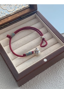 Detail of red braided cord bracelet with silver gourd charm and Fu character engraving