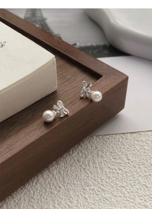 Detail of silver bow pearl earrings placed on a dark wood tray near white books