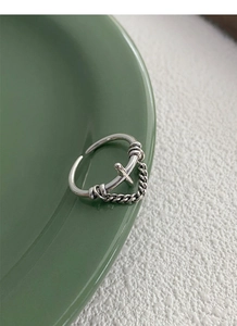 Close-up of S925 sterling silver ring with cross design and chain detail on ceramic plate