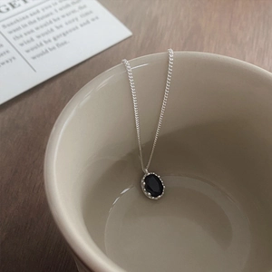 925 sterling silver necklace with oval black zircon pendant on a beige ceramic cup
