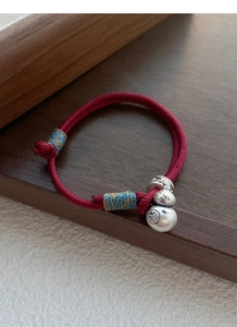 Detail of red braided rope bracelet with silver gourd pendant and Fu character engraving