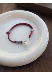 Detail view of S999 silver gourd charm on handmade red woven rope bracelet with lucky beads