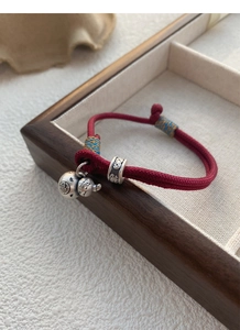 Detail of red braided bracelet with silver calabash charm and lucky coin pendant