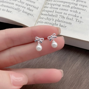Elegant S999 silver bow earrings with round pearls shown in a lifestyle hand-held shot