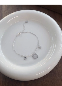 Detail of S925 sterling silver daisy bracelet with floral charms on a ceramic plate