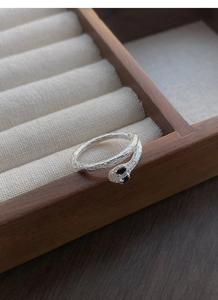 Macro detail of silver snake ring with black stone eyes and textured scales on wood