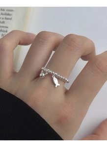 Gros plan d'une bague en perles d'argent S925 avec charms poisson et boule sur le doigt