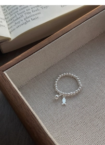 Détail d'une bague en perles d'argent avec breloque poisson sur une surface en lin