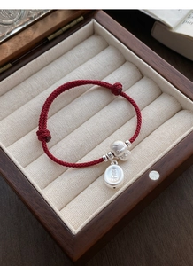 Detailed shot of S925 silver charms on red woven bracelet inside a premium wooden box
