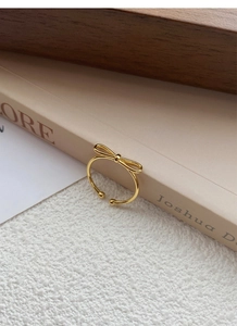 Detail shot of a minimalist gold bow ring with adjustable open band on a warm background