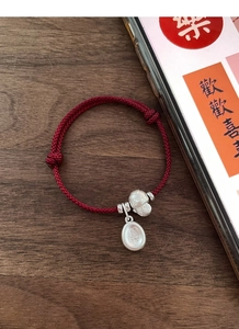 Detail showing red woven cord bracelet with silver fortune cat and engraved joy charm