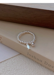Détail de bague en perles d'argent S925 avec breloques poisson et boule posée sur un livre