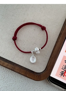 Detailed shot of red woven bracelet with silver Fortune Cat and 'Joy' charms