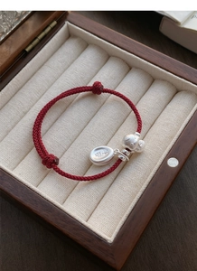 Macro detail of red woven S925 silver bracelet with Ping An and fish charm on velvet