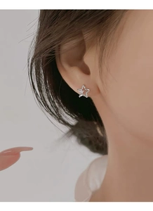 Close-up of S999 sterling silver star stud earring with zircons on model ear