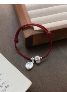 Detail of red braided silver bracelet with Fu and Le charms on dark wooden jewelry box