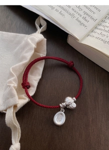 Detail of red braided silver bracelet with lucky pendants and bell on rustic background