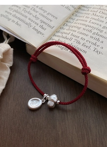 Detail of red braided bracelet with silver charms featuring Fu and Le characters