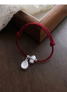 Close-up of red woven bracelet with silver lucky bag and Xile character charms
