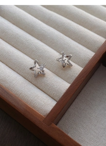 Close-up of S999 sterling silver star earrings with zircons on a beige jewelry cushion