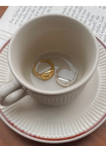 Close-up of minimalist gold and silver open rings with hollow oval curves on a ceramic cup