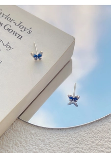 Dettaglio di orecchini a farfalla blu in argento S999 fissati su un libro