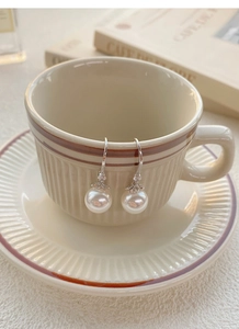 Détail de boucles d'oreilles en argent S999 et perles sur le bord d'une tasse en café