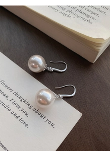 Détail de boucles d'oreilles en perles argent S999 avec zircon sur un livre ancien