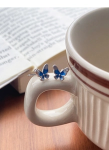Dettaglio degli orecchini a perno a farfalla blu in argento su un manico di tazza