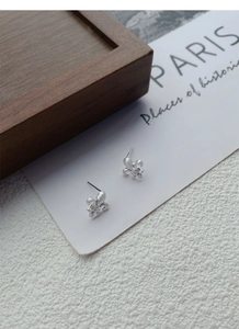 Macro view of fleur-de-lis silver earrings with brushed texture and tiny central crystal