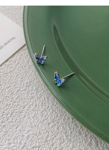 Dettaglio degli orecchini a farfalla in smalto blu su un piatto di ceramica verde