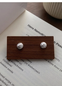 Detail of brushed S925 sterling silver starburst studs on dark wood display with book