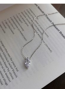 Marquise-cut crystal pendant on a silver chain displayed over vintage book pages