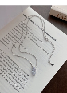 Detail of S925 sterling silver necklace featuring marquise cut diamond pendant on book