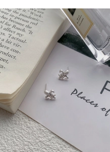 Macro shot of silver fleur-de-lis earrings with matte texture and small diamonds