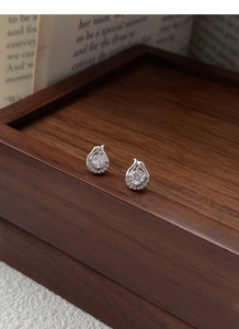 Macro shot of silver teardrop stud earrings with zircon inlay on dark wooden box