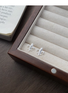 Detailed macro view of silver fleur-de-lis earrings with diamonds on a wooden jewelry box
