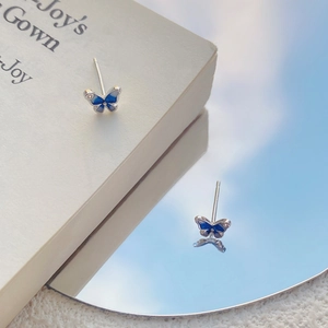 Orecchini a perno a farfalla blu in argento S999 su libro con riflesso del cielo nello specchio