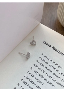 Macro shot of silver bow heart earrings with zircons on an open book background